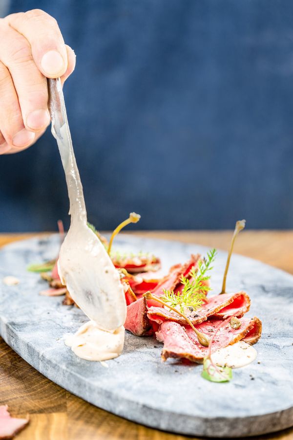 Für das Vitello tonnato wird Thunfischsauce neben das drapierte Fleisch gegeben