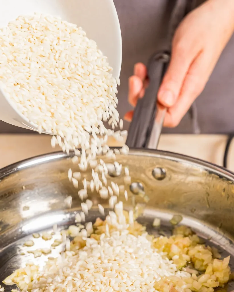 Risotto-Reis wird aus einer Schüssel in eine Pfanne gegeben.