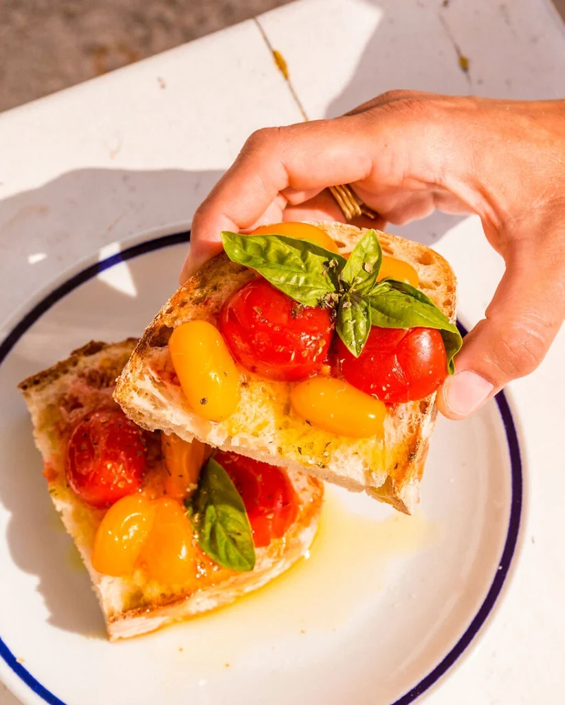 in der Sonne Kampaniens nimmt sich eine Hand eine Scheibe Bruschetta mit reifen und aromatischen Datteltomaten