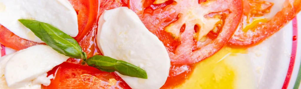 Nahaufnahme eines Tellers mit Caprese oder Tomate Mozzarella, man sieht im Detail die Tomatenscheiben, Scheiben von Mozzarella und ein paar Träufel von Olivenöl