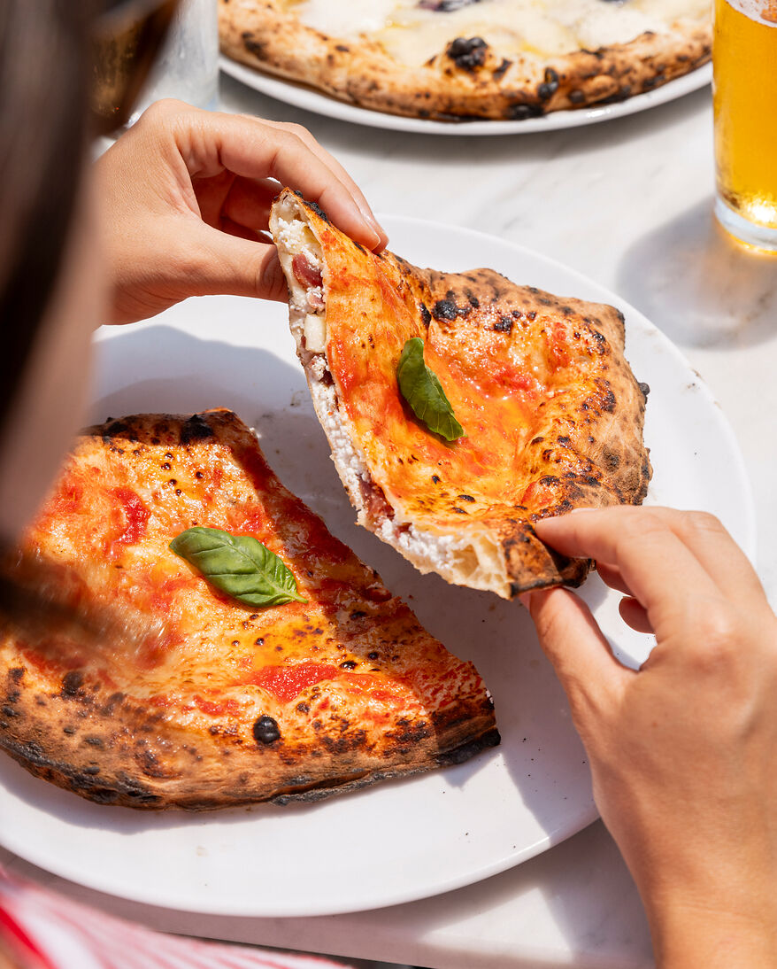 eine Frau ist kurz davor in eine frische neapolitanische Calzone zu beißen, zu sehen ist die Füllung der Calzone