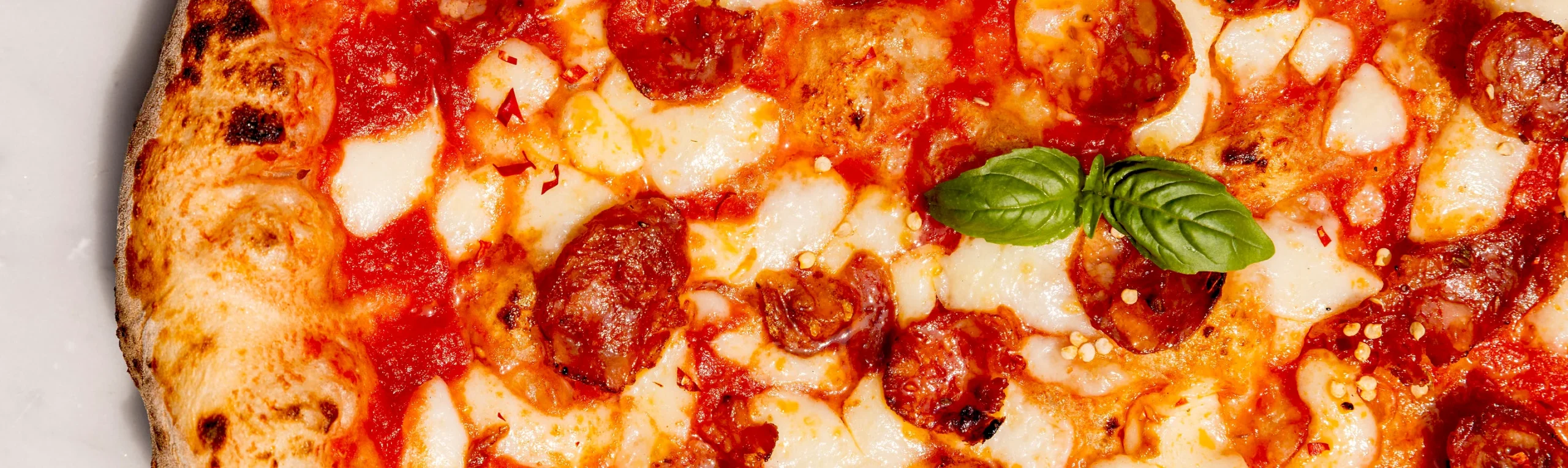 Nahaufnahme einer Pizza Diavola, alle Zutaten sind gut zu erkennen: Tomatensoße, Fior di Latte, scharfe Salami und Chiliflocken