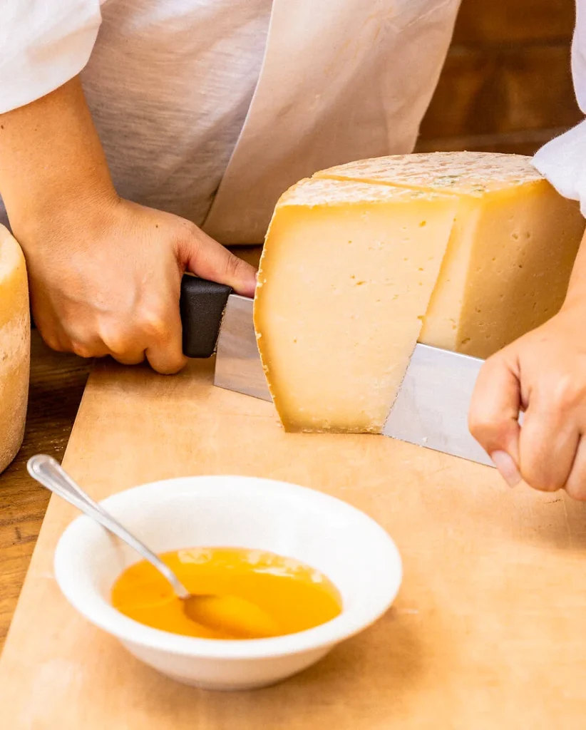 auf einem großen Holzbrettchen wird ein ganzer Laib Pecorino mit einem Messer in Stücke geteilt.