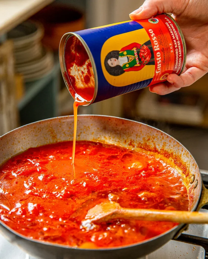 eine Hand hält eine Dose mit San Marzanotomaten in der Hand, welche ich die Pfanne gegossen werden, um ein Sugo zu kochen