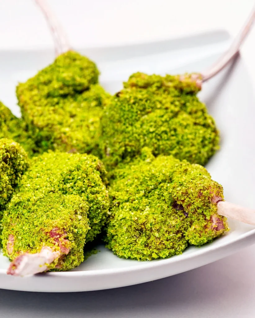 auf einem weißen Teller liegen die vorbereiteten panierten Lammkoteletts, fertig für die Weiterverarbeitung