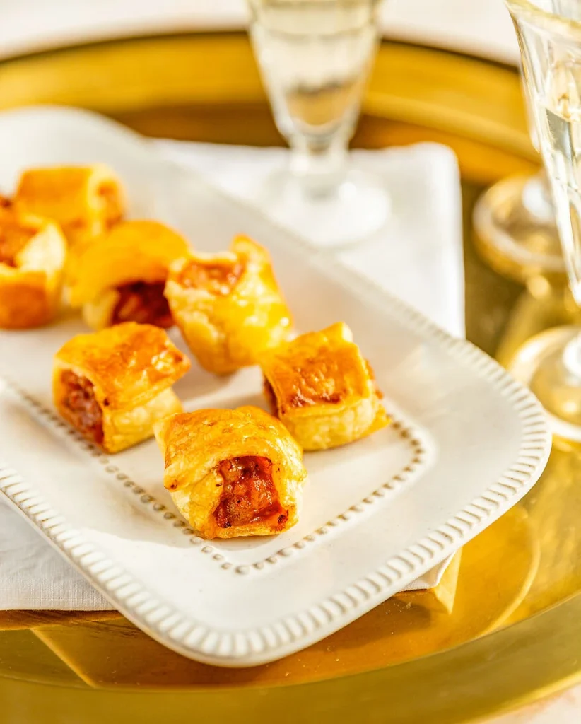 iatlienische Würstchen im Schlafrock mit Salsiccia auf einem weißen Teller, serviert auf einem goldenen Tablet mit Serviette und Gläsern