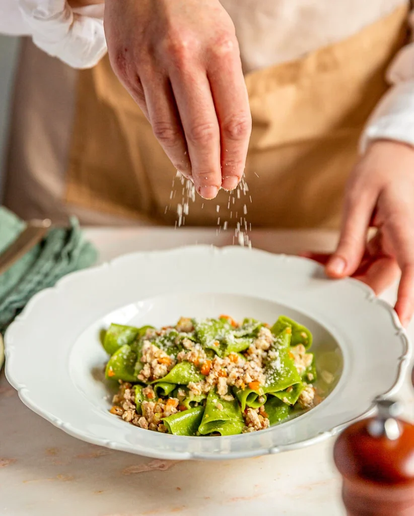 in einem tiefen Teller werden frisch gekochte grüne Pappardelle mit Ragu Bianco mit Parmesan garniert