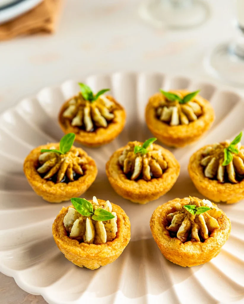 kleine Parmesantörtchen aus Mürbeteig werden auf einem weißen Teller serviert, Topping aus Balsamico di Modena