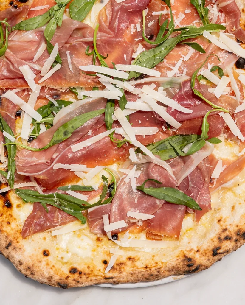 Nahaufnahme einer Pizza Proscuitto neapolitana aus der Draufsicht: Man sieht den rohen Schinken gut