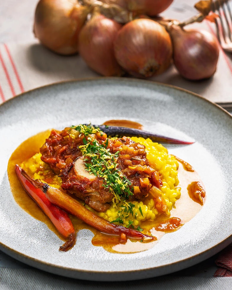 Ossobuco alla Milanese mit Safranrisotto und glasierten Möhren serviert auf einem grauen Steinzeugteller