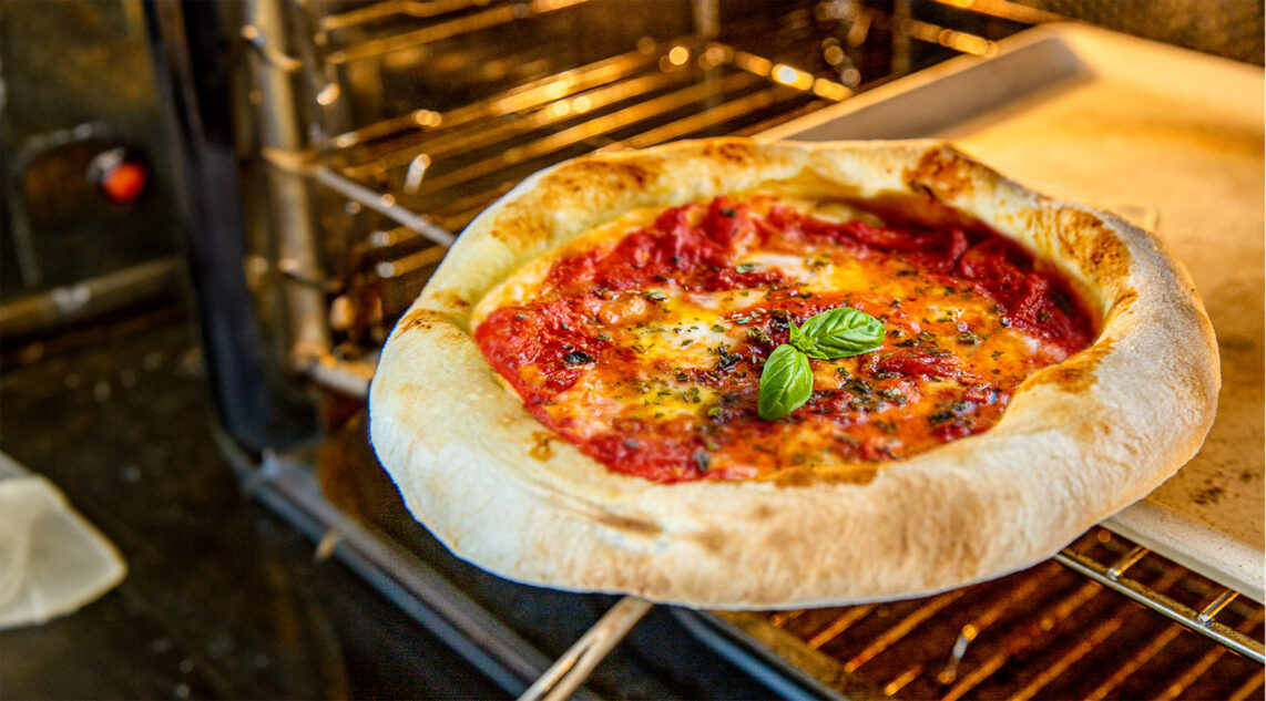 eine frisch gebackene Pizza wird mit Hilfe eines Pizzaschiebers aus dem heimischen Backofen gehoben