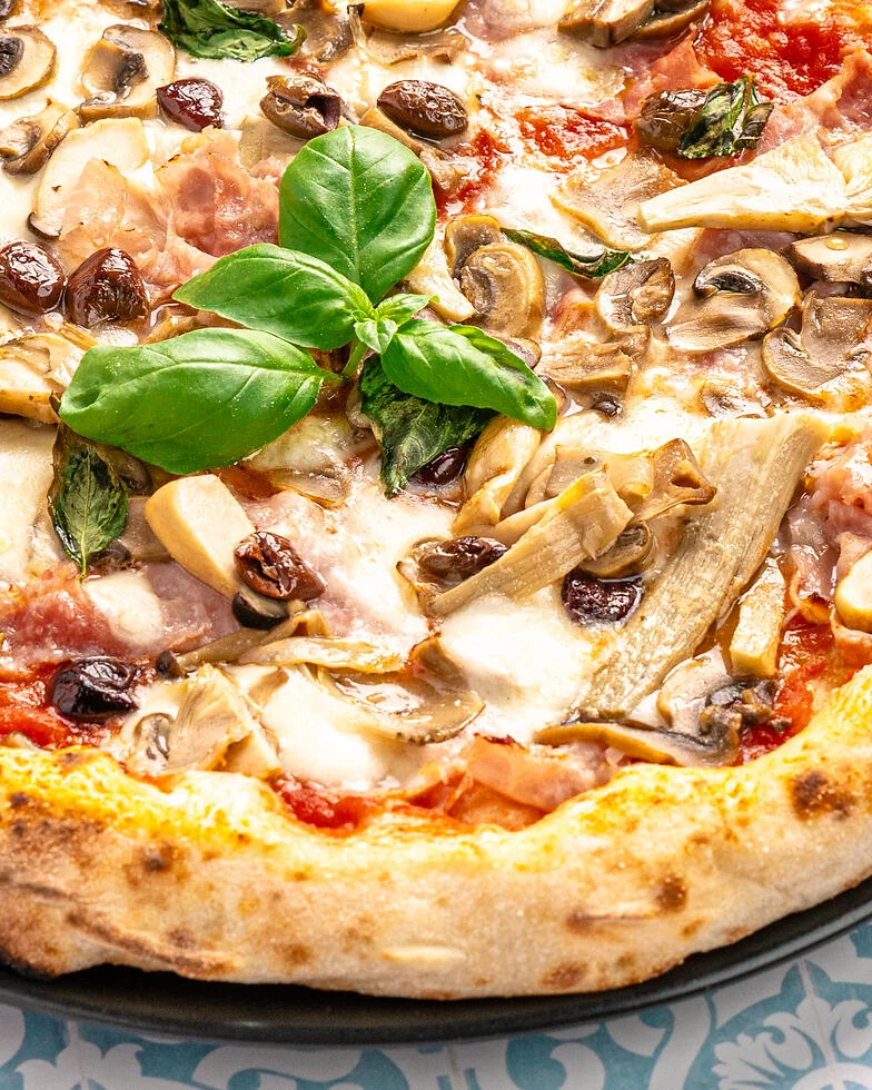 nahaufnahme einer Pizza Capricciosa mit Schinken, Artischokenherzen, Champignons und Oliven