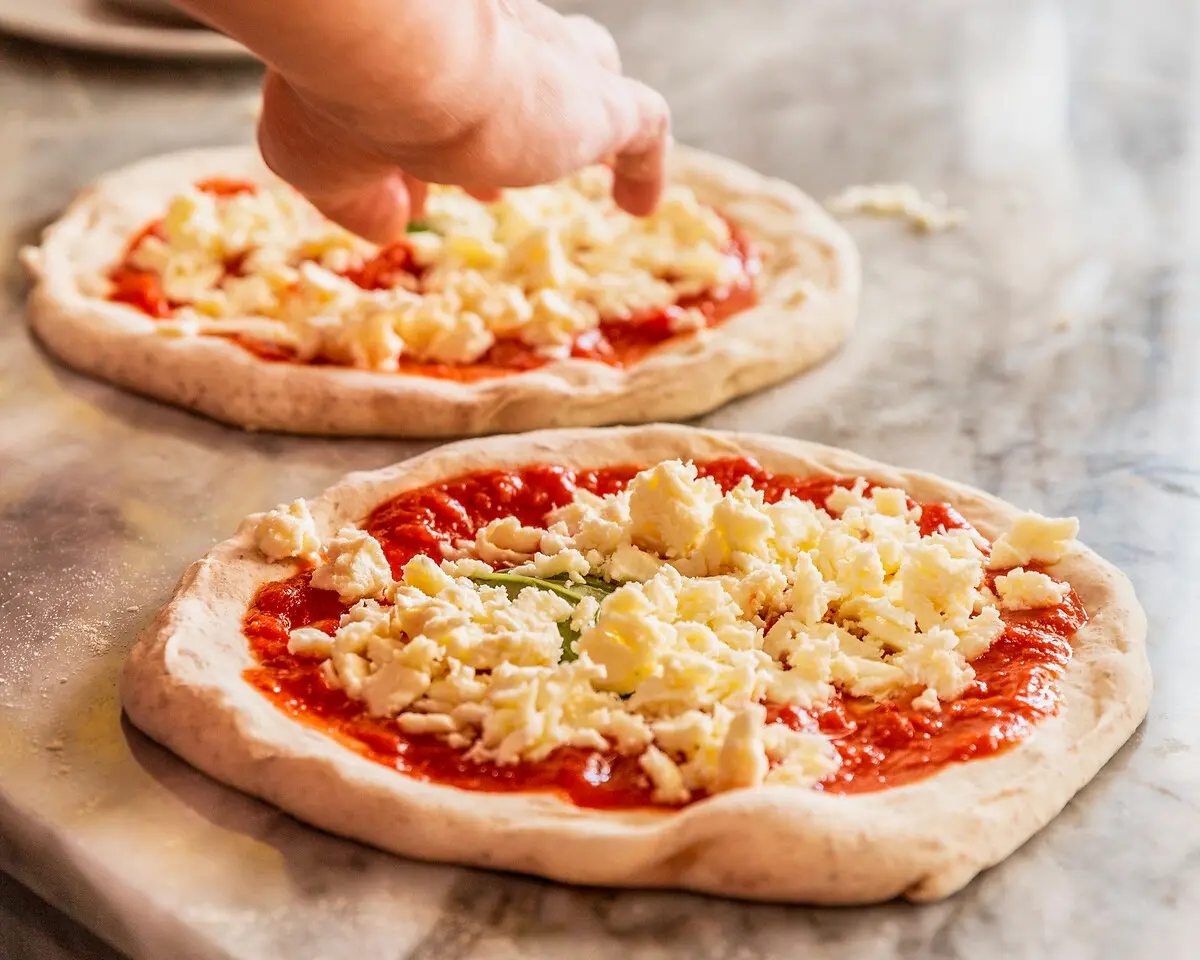 ein Pizzaiolo verteilt Fior di Latte auf einer Pizza