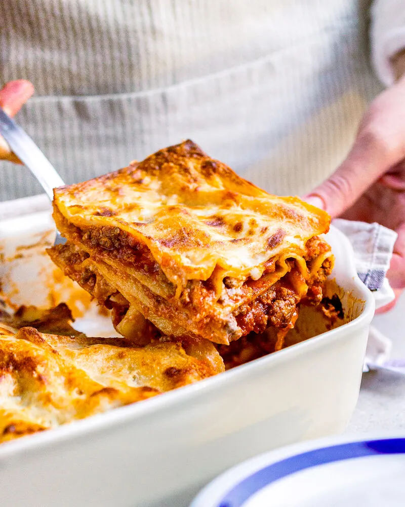 frische Lasagneplatten zum Kochen, Hand hebtmit einem Pfannenwender die fertige Lasagne aus der Ofenform