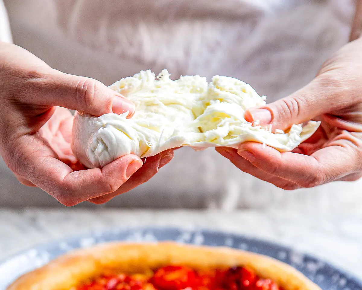 zwei Hände rupfen eine Kugel Büffelmozzarella auseinander, die innere Struktur ist gut zu erknennen