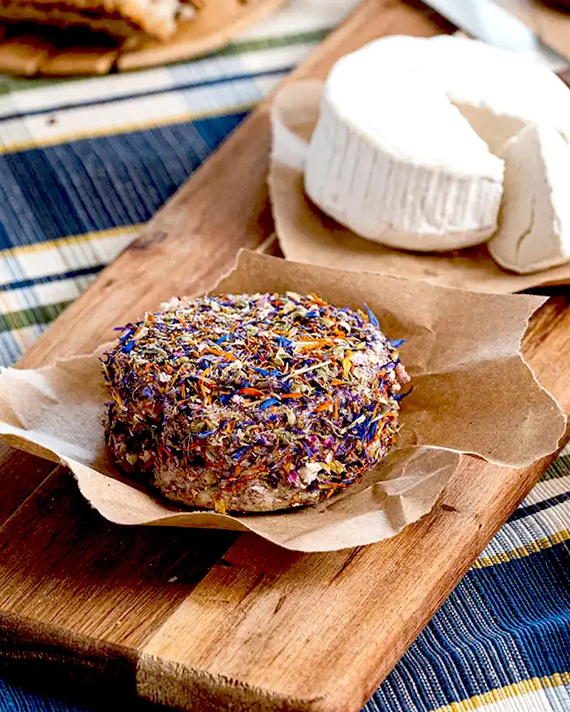 Fiori Eduli - vegane Käsealternative mit Blüten, Bio veganer Käse mit Blütenmantel liegt auf einem Holzbrettchen, Fiori Eduli