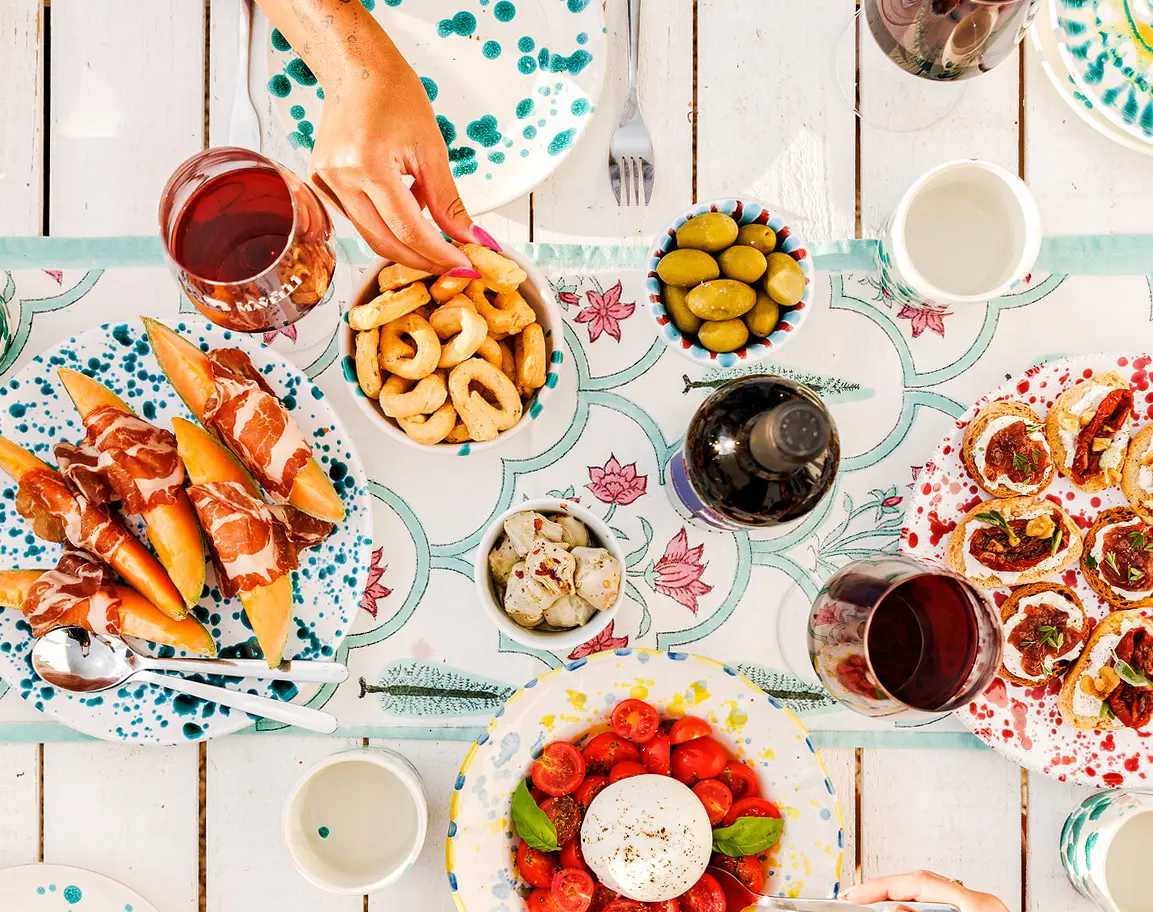zu sehen ist ein weißer Holztisch, der mit vielen leckeren italienischen Antipasti und Wein gedeckt ist