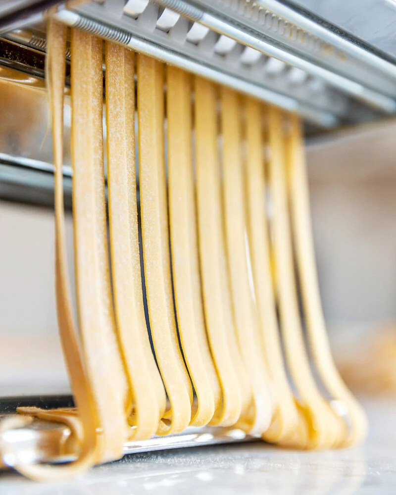 aus einer Pastamaschine kommen frische Bandnudeln